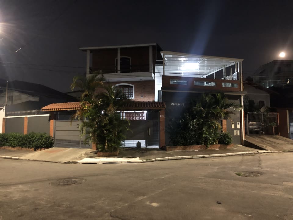 A casa vista da esquina à noite, com o número 310 no portão e palmeiras na calçada.